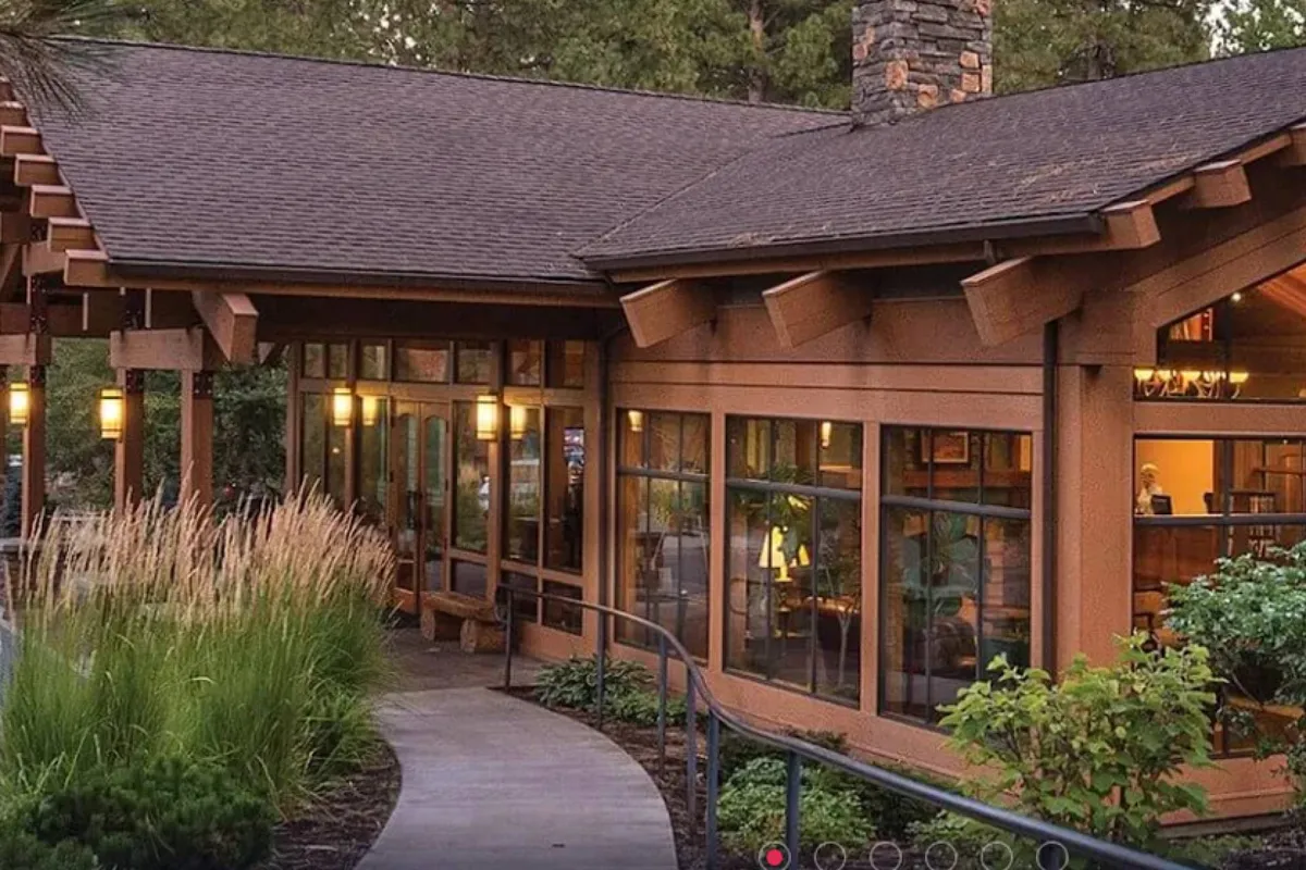 This inviting exterior shot displays wooden resort architecture with large glass windows set amidst beautifully landscaped greenery. Children are playing in the yard, and families are gathering, reflecting the playful, welcoming resort environment.