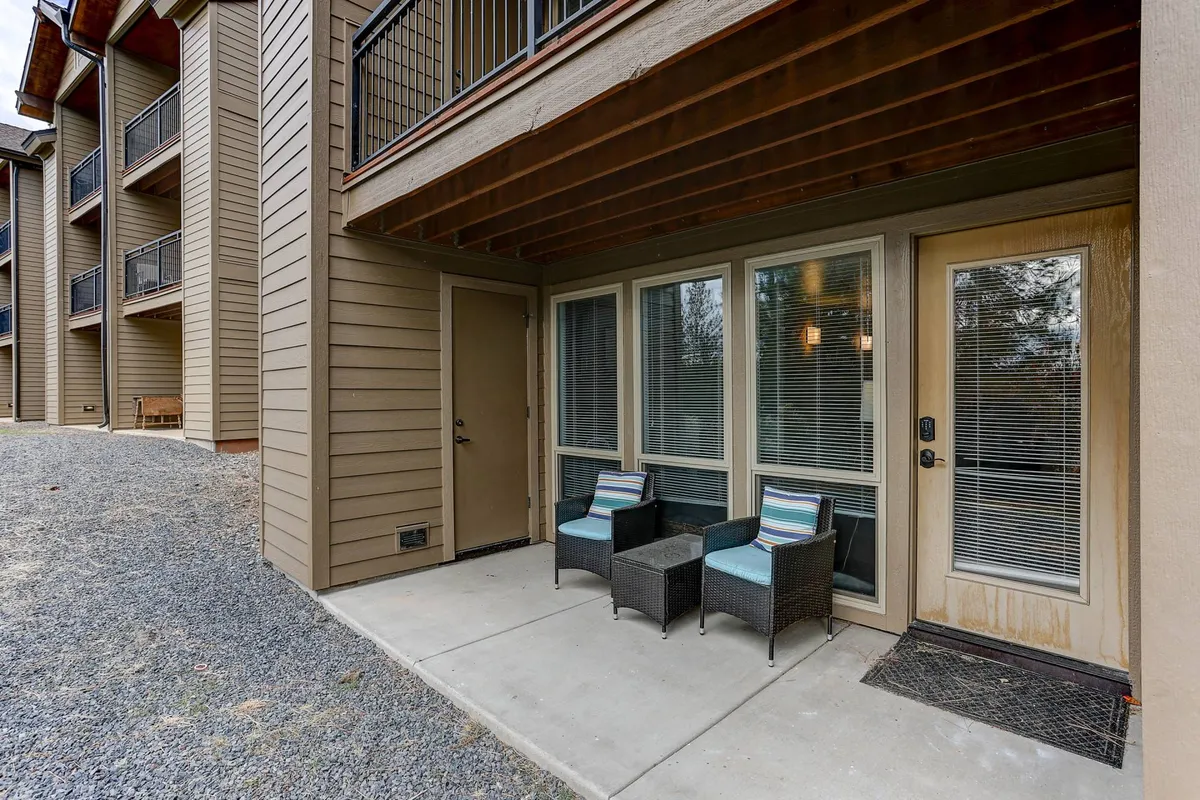 This image features a pair of inviting wicker chairs with cushions set on a private patio, just outside a glass door that leads inside. The morning light illuminates the space, suggesting a perfect spot to enjoy coffee or relax while taking in the tranquil surroundings.
