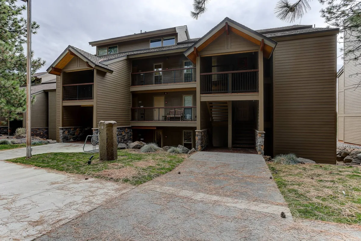 This image showcases the welcoming wooden architecture of the resort building, enhanced by stone accents and attractive landscaping. People can be seen enjoying the outdoor environment, with opportunities for walking or biking in the area, which hints at the family-friendly and communal atmosphere.