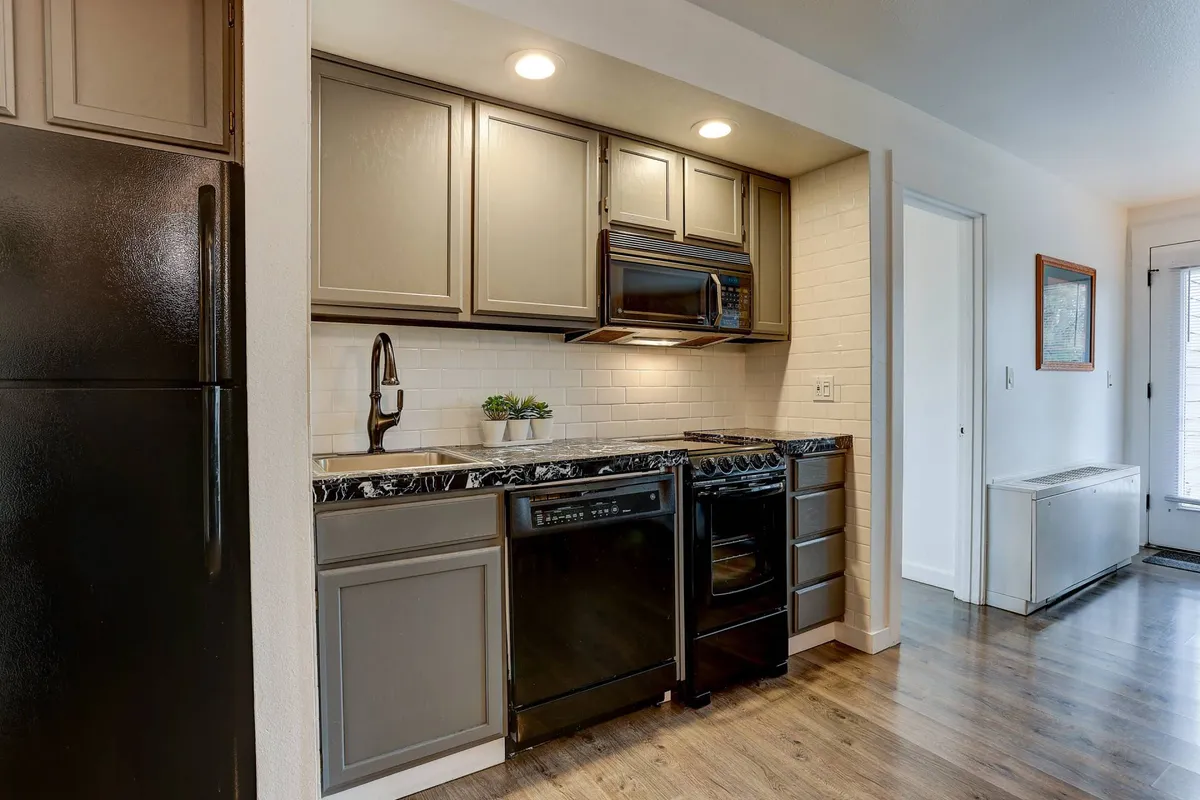 A modern kitchen scene with black appliances, marble countertops, and grey cabinetry, bathed in natural light from a window. The counters are spacious, inviting meal preparation and group gatherings.