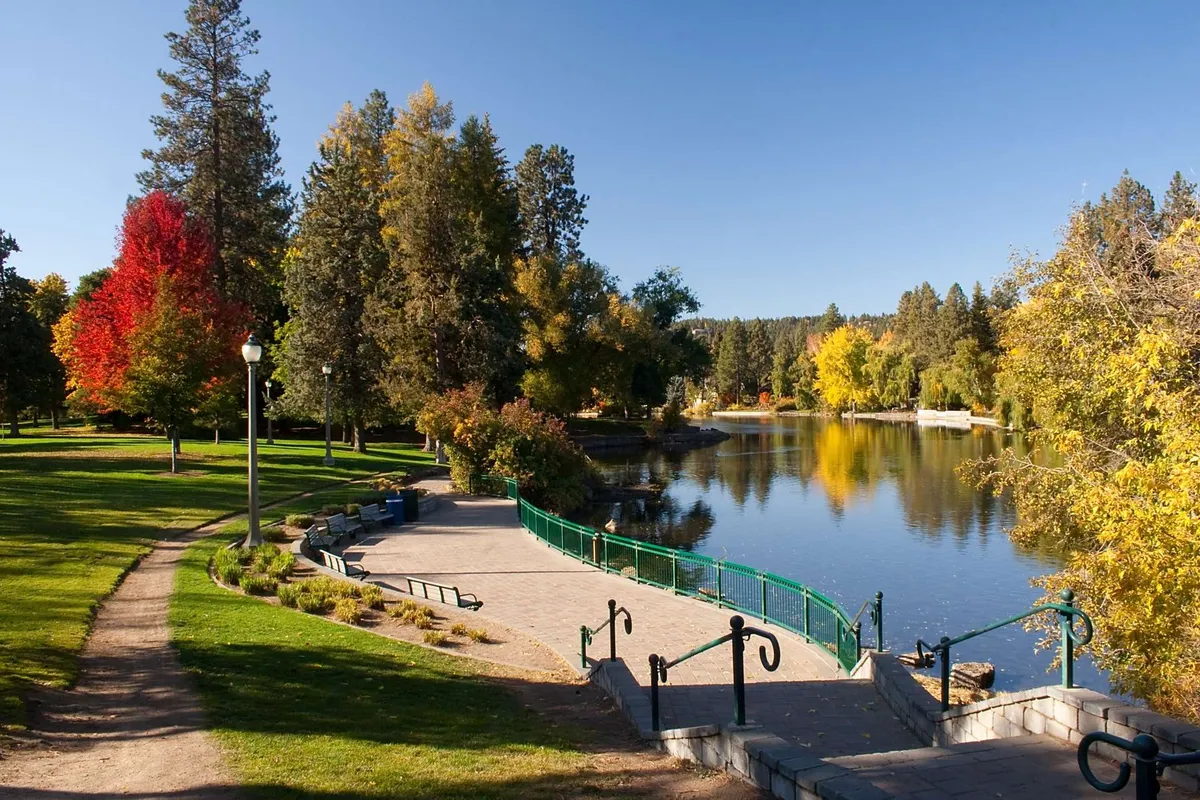 A serene lakeside scene with colorful trees, a gentle walking path, and a charming bridge. The calm water and natural beauty invite activities like family walks, picnics, and quiet moments together, capturing the year-round enjoyment available at the resort.